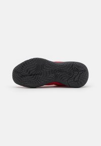 Semelle d'une chaussure de sport rouge avec une texture en caoutchouc noir pour une meilleure adhérence et le logo Puma près du talon sur un fond blanc.