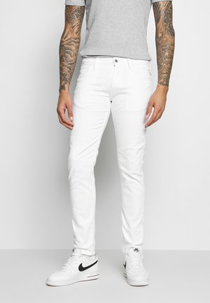Weiße Jeans mit schlankem Schnitt, aus elastischem Baumwollstoff gefertigt. Mit einem vorderen Knopfverschluss und Gesäßtaschen, getragen mit weißen Sneakers.