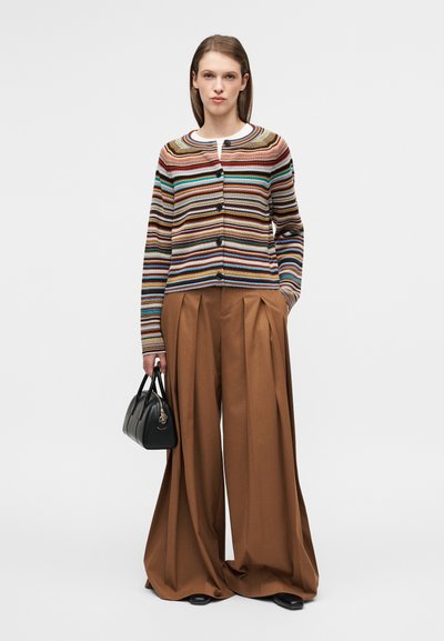 Ριγέ ζακέτα με πολλαπλά χρώματα, στρογγυλή λαιμόκοψη και κουμπιά στο μπροστινό μέρος, συνδυασμένη με καφέ παντελόνια φαρδιάς γραμμής και μια μικρή μαύρη τσάντα.