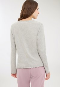 Maglietta grigia chiara a maniche lunghe con scollatura rotonda, orlo ondulato e polsini. Il tessuto sembra morbido e leggero.