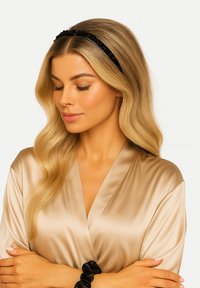 Czarna satynowa opaska do włosów z marszczonymi detalami. Modelka ma na sobie beżowy satynowy szlafrok, prezentujący gładką fakturę i miękki połysk.