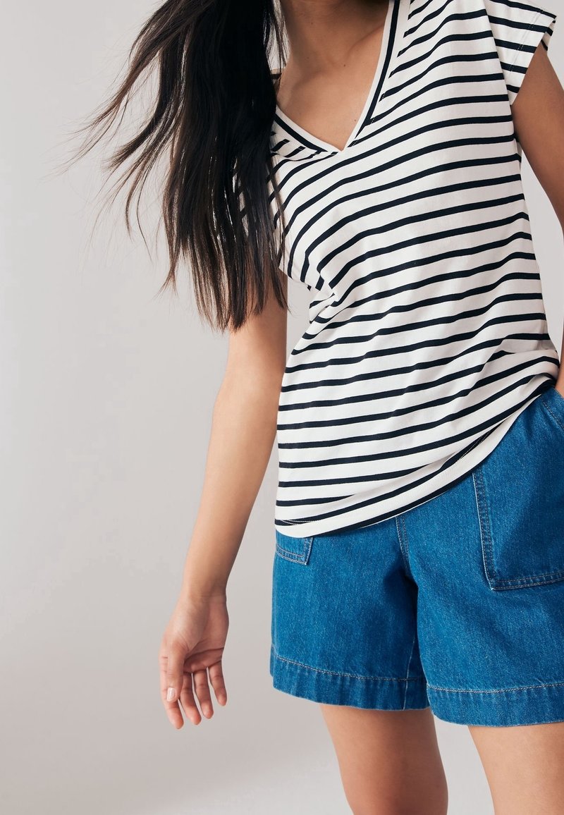 Personne portant un t-shirt à manches courtes rayé blanc et noir avec un short en denim bleu, avec de longs cheveux foncés partiellement visibles.