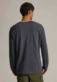 Koszula z długim rękawem i okrągłym dekoltem w ciemnoniebieskim kolorze z delikatną fakturą i wielokolorowymi muszkami; zestawiona z khaki spodniami cargo.