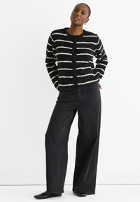 Gestreifter schwarzer und weißer, flauschiger Cardigan mit rundem Halsausschnitt und Knopfverschluss, kombiniert mit hochgeschnittenen schwarzen Weitbeinjeans.