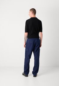 Black short-sleeve shirt paired with navy blue cargo pants featuring side pockets. Material appears breathable; pants have a relaxed fit.
