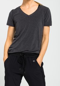 T-shirt noir à col en V en tissu léger, avec des manches courtes et une coupe décontractée, associé à un pantalon noir à cordon de serrage.