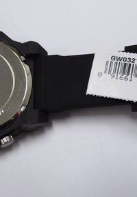 Montre avec un bracelet en caoutchouc noir, un boîtier métallique rond, une surface lisse et une étiquette de prix visible. Dos en métal, design minimaliste, construction robuste.