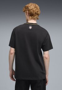 Sort bomulds t-shirt med korte ærmer, der har rund halsudskæring og en mærkat på øverste del af ryggen. Stoffet ser glat ud uden synlige mønstre.