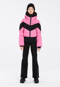 Doudoune rose et noire avec un design en chevrons, dotée d'un col haut et d'une fermeture éclair à l'avant. Pantalon noir avec une texture en pied-de-poule, associé à des bottes noires.