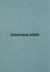 Light blue cotton fabric featuring the text "REDEFINED REBEL" in bold black font, centrally located on the material's surface.