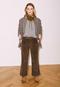 Pantalons en velours côtelé marron à jambes larges, t-shirt gris, blazer en chevron, écharpe marron, bracelets en superposition et bottines beiges.