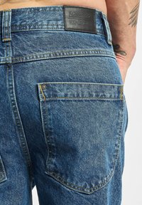 Jeans de mezclilla en un lavado azul medio con una superficie texturizada, que cuentan con una etiqueta de cuero, costuras en contraste y un detalle en el bolsillo trasero.