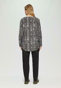 Langsleeve blouse met een grijs en zwart slangenprintpatroon, zachte stof, ronde zoom, gecombineerd met zwarte broek en groenachtig bruine schoenen.