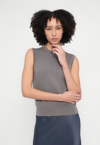 Pelēks adīts bezroku tops ar ribotu apkakli un apakšu, saskaņots ar gludu tumši zilu svārku. Mīksta tekstūra ar minimālām detaļām.