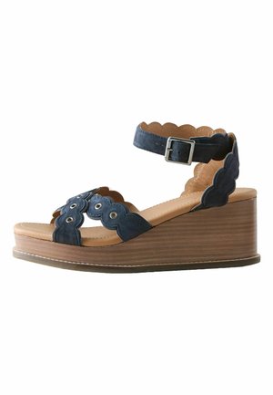 Kiilkinga tumesiniste laineliste seemisnahast rihmade ja hõbedase pandlaga, pruunikaskollase polsterdatud sisevoodri ja pruun puidust platvormkontsaga.