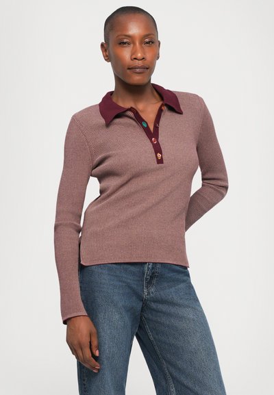 Ribbede, mauve langermede polo genser med burgunder krage og knappestolpe. Bært med blå denim jeans med en tettsittende design.