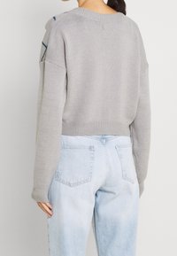 Harmaa neulottu villapaita, jossa on rento leikkaus, roikkuu hartiat ja ribbireunukset, yhdistettynä vaaleansinisiin farkkuihin.