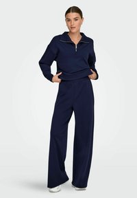 Sweatshirt bleu marine avec un col zippé mi-haut, des poignets élastiques et un pantalon large assorti en tissu doux.