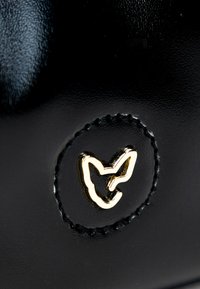Scarpe in pelle nera con un cerchio che presenta un logo di una volpe con contorno dorato, accentuate da dettagli di cucitura a contrasto.