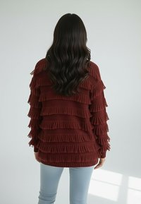 Bordowy sweter z dzianiny z warstwowymi frędzlami, długimi rękawami i luźnym krojem, zestawiony z jasnoniebieskimi dżinsami.