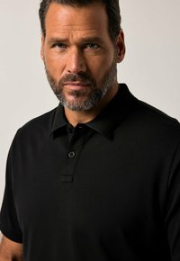 Sort polo-shirt med et enkelt design, korte ærmer og en to-knaps knaplukning. Fremstillet af åndbart stof med en struktureret overflade.