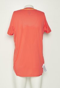 Camisa deportiva de manga corta en color coral con cuello redondo, textura de malla, aberturas laterales y una etiqueta en la parte inferior derecha.