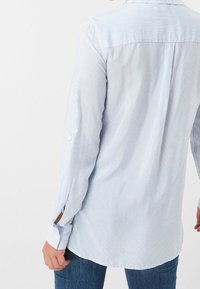 Camicia a maniche lunghe blu e bianca a righe con un orlo leggermente curvo e linguette sui polsi con bottoni. Realizzata in tessuto leggero.