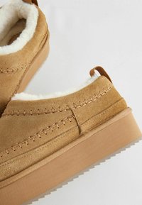 Tamne natika cipele od suede s mekanim bijelim krznom iznutra i debelim platformama s nazubljenim rubom. Vidljivi detalji šivanja.