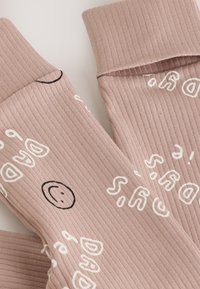 Gerippte rosa Socken mit weißem Text und einem schwarzen Smiley, mit umgeschlagener Manschette für zusätzlichen Detailreichtum und Textur.