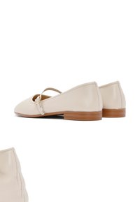 Beige leather flats with an open cutout, back strap, and small heel. Smooth texture, minimal stitching, and a simple round toe design.