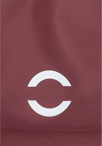 Superficie di tessuto bordeaux con una texture liscia presenta un logo circolare bianco prominente al centro, progettato con uno stile minimalista.
