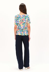 Top peplum floral con mangas cortas, que presenta colores vibrantes como el rosa y el amarillo, combinado con pantalones de pierna ancha en color marino y tacones bajos.