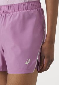 Lilla treningsshorts laget av lett stoff med elastisk midjebånd. Har sidespalter og en liten logo på kanten.