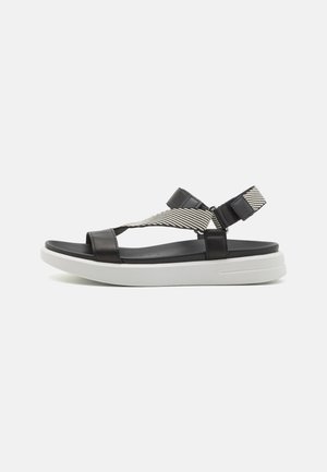 Sandalias de tiras de cuero negro con suela de espuma blanca, que presentan una banda elástica a rayas en la parte superior y una correa ajustable en el tobillo para un mejor ajuste.