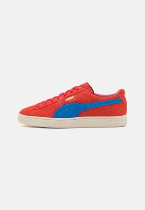 Basket Puma en daim rouge bas avec bande bleue dentelée et semelle beige, vue de côté.