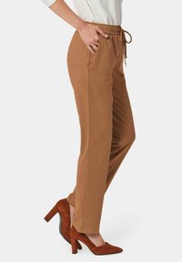 Pantalons marron ajustés avec une taille élastique et un cordon de serrage. Présente des poches latérales et une texture lisse et douce. Accompagnés de talons hauts rouges.