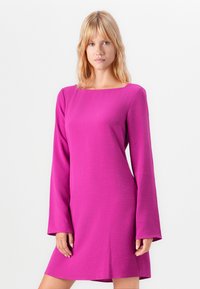 Fuksiapinkki pitkähihainen mekko, jossa on neliöomainen kaula-aukko, teksturoitu kangas ja suora siluetti, joka ulottuu polven ylle. Sileä, pehmeä pinta.