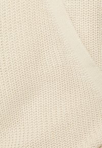 Tessuto in maglia color crema con una leggera trama a coste. Presenta un elemento di design diagonale, che crea profondità visiva.