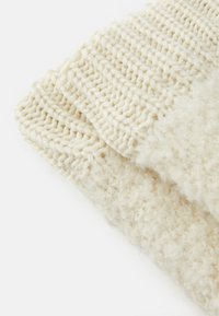 Tissu tricoté couleur crème montrant deux couches texturées, l'une avec un motif côtelé lisse et l'autre avec une apparence duveteuse.