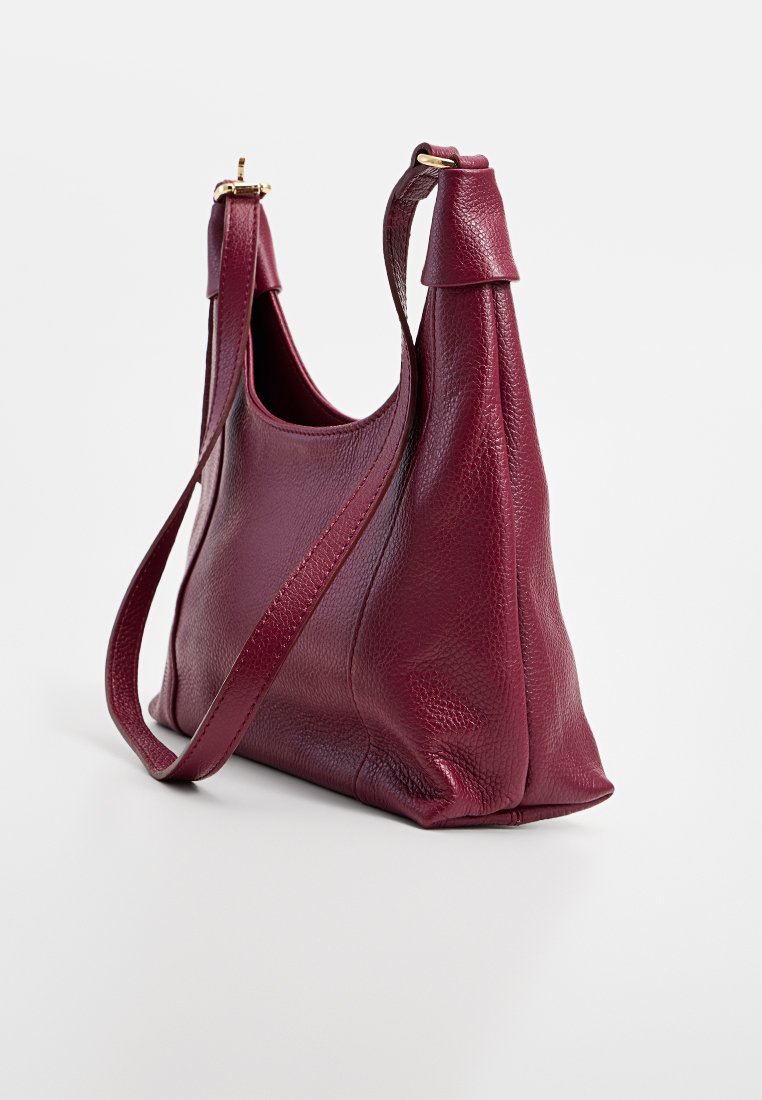 Sac à main en cuir bordeaux avec une texture lisse, une forme structurée, deux poignées courtes et une longue bandoulière réglable.