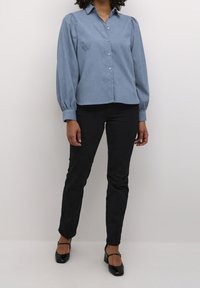Camisa de botones azul claro con cuello y mangas abullonadas, combinada con pantalones negros y zapatos de tacón negros. Textura suave en todo.