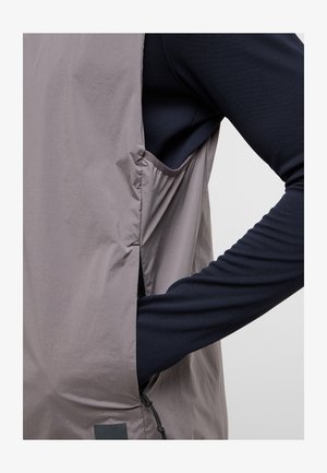 Lichte, grijze buitenlaag met een zachte textuur, voorzien van een zijzak en een aansluitende marineblauwe lange mouw basislaag eronder.