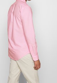 Ljust rosa skjorta med lång ärm som har vita vertikala ränder, knäppbar krage, knappade manschetter och rundad nederkant. Avslappnad design med mjuk textur.