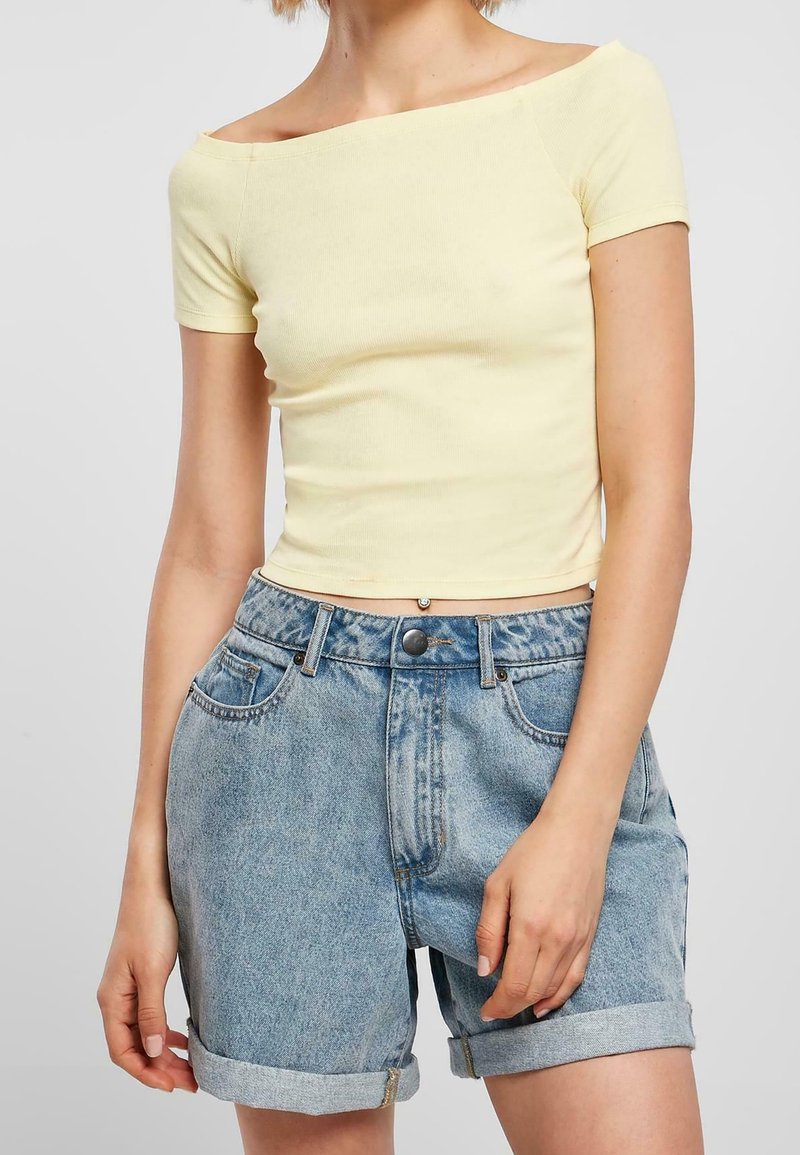 T-shirt ajusté jaune à épaules dénudées, associée à un short en jean bleu clair, présentant des ourlets retroussés et un design classique à cinq poches.