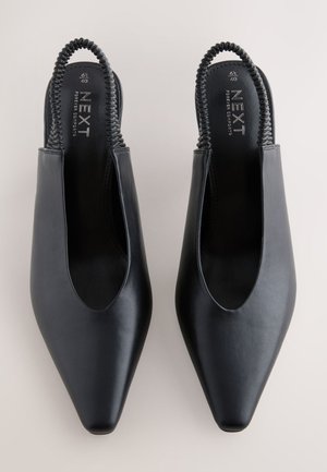 Chaussures slingback en cuir noir avec un bout pointu, des côtés ouverts et une bride tressée à l'arrière. Texture lisse et design minimaliste.