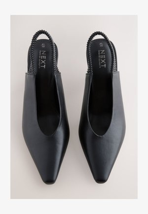 Chaussures slingback en cuir noir avec un bout pointu, des côtés ouverts et une bride tressée à l'arrière. Texture lisse et design minimaliste.