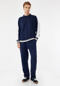 Granatowy sweter z białymi rękawami, w paski na mankietach oraz dopasowane granatowe spodnie dresowe. Posiada luźny krój i miękką tkaninę dla komfortu.