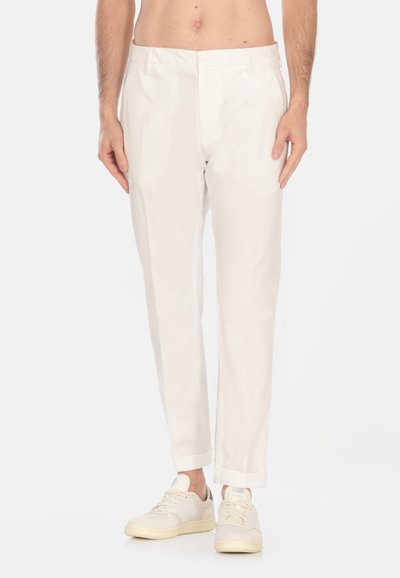 Pantaloni bianchi su misura con una vestibilità slim, dotati di frontale piatto, tasche laterali e risvolti, abbinati a sneaker di colore chiaro.