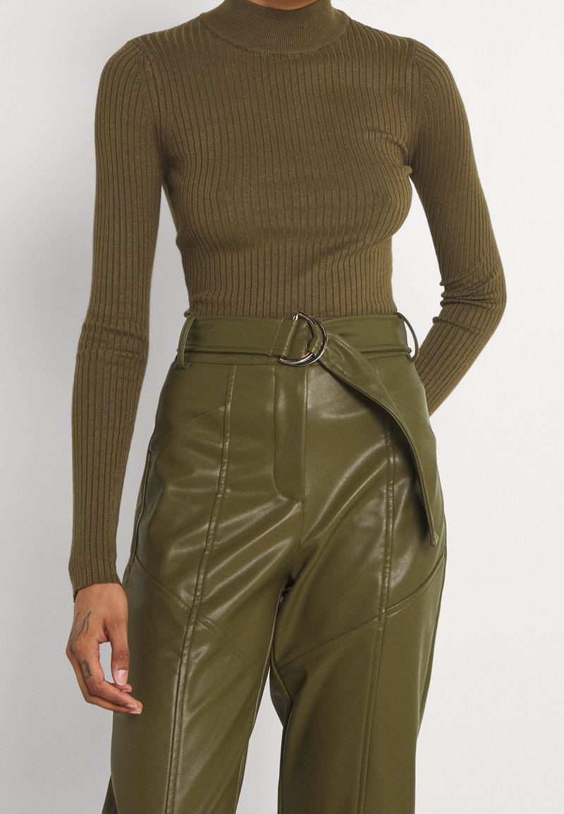 Pull en maille côtelée de couleur vert olive avec un col roulé et des manches longues, associé à un pantalon en simili cuir taille haute avec un détail de boucle en argent ronde.