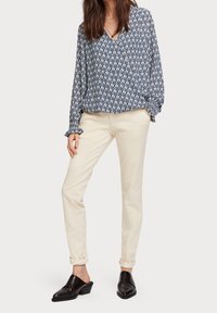 Blusa a maniche lunghe navy e bianca con motivo e maniche a volantino, abbinata a pantaloni fitted color crema e mule neri senza lacci.